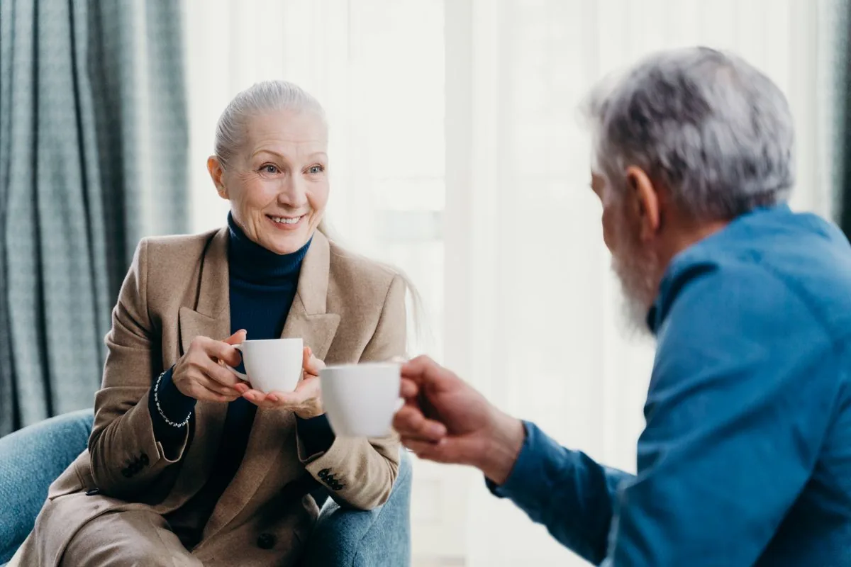 Two seniors chatting warmly over coffee at home