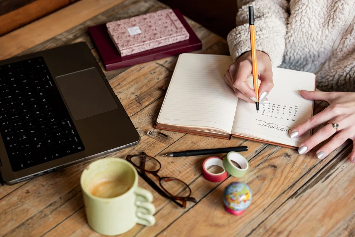 Hands writing plans and notes in a notebook on a wooden desk