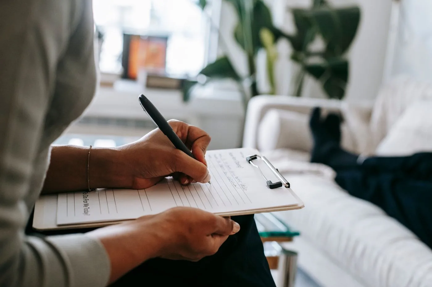 A person writing notes on a clipboard in a bright living room